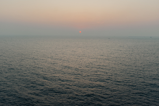 View of the sun s crimson orb sinking into the tranquil dark waters of the Arabian Sea under a hazy sky casting a serene glow Chiplun Maharashtra India. View of the sun s crimson orb sinking into the tranquil dark waters of the Arabian Sea under a hazy sky casting a serene glow Chiplun Maharashtra India.