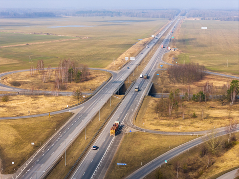 Aerial view of a highway interchange with trucks and cars driving through flat rural fields and bare trees Lithuania.