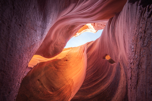 View of smooth sculpted sandstone walls curve and twist a dance of light and shadow leading the eye to a glimpse of the sky above Escalante Utah United States.