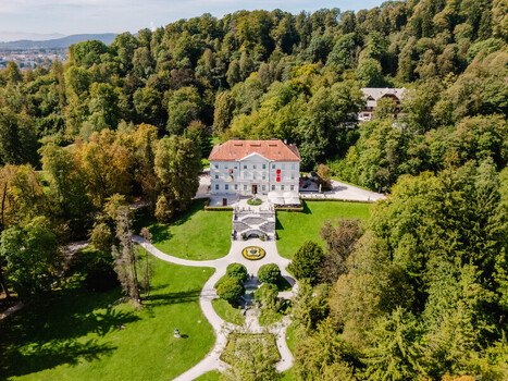 Aerial view of Tivoli Mansion surrounded by lush green trees manicured lawns and stone pathways in Tivoli Park in Ljubljana Slovenia.
