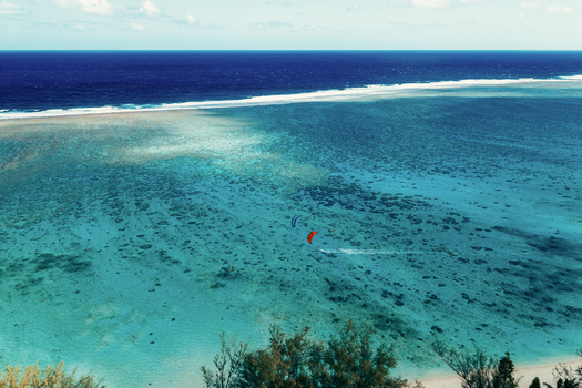 Aerial view of a kite surfer gliding over the turquoise lagoon and coral reef of Rarotonga Cook Islands. Aerial view of a kite surfer gliding over the turquoise lagoon and coral reef of Rarotonga Cook Islands.