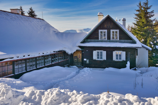 View of a snow covered cottage with dark wood contrasting against the bright white snow and a clear blue sky above in Donovaly Banskobystricky kraj Slovakia. View of a snow covered cottage with dark wood contrasting against the bright white snow and a clear blue sky above in Donovaly Banskobystricky kraj Slovakia.