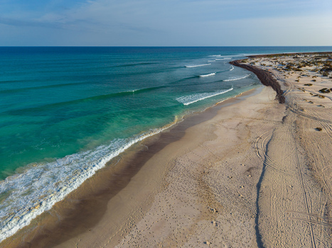 Aerial view of turquoise waves gently washing onto the pristine sands of Aomak campsite where the desert meets the ocean Aomak campsite Socotra Yemen.