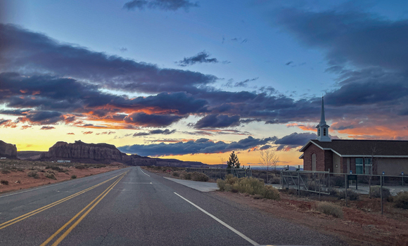 View of a road leading towards the iconic buttes of Monument Valley Tribal Park under a dramatic sunset sky in Oljato Monument Valley Utah United States.