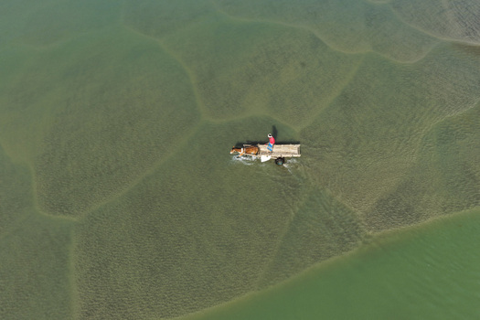 Aerial view of a person driving a horse drawn cart through shallow clear water with visible sand patterns in Joypurhat Rajshahi Division Bangladesh. Aerial view of a person driving a horse drawn cart through shallow clear water with visible sand patterns in Joypurhat Rajshahi Division Bangladesh.