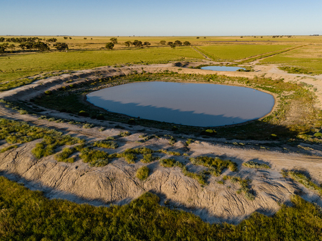 Aerial view of a flat landscape featuring a circular water dam surrounded by dry earth and green pastures in Hay New South Wales Australia.