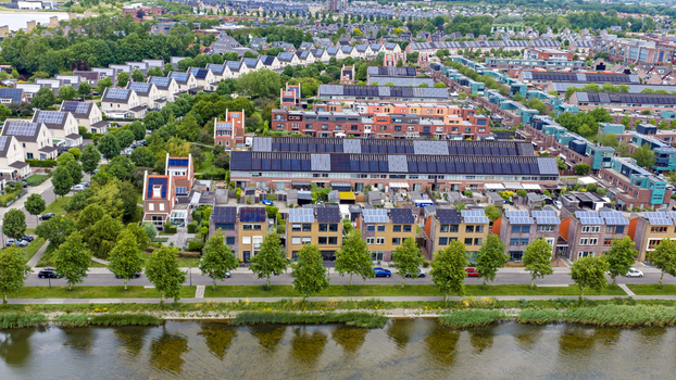Aerial view of modern residential houses with solar panels on rooftops along a canal and green trees in Heerhugowaard North Holland Netherlands. Aerial view of modern residential houses with solar panels on rooftops along a canal and green trees in Heerhugowaard North Holland Netherlands.