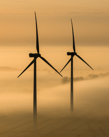 Aerial view of towering wind turbines pierce through a sea of ethereal fog their silhouettes stark against the muted dawn Wislina Pomeranian Voivodeship Poland. Aerial view of towering wind turbines pierce through a sea of ethereal fog their silhouettes stark against the muted dawn Wislina Pomeranian Voivodeship Poland.