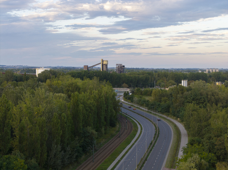 Aerial view of a winding road and railway tracks passing through lush green trees with industrial buildings in the distance under a cloudy sky in Krakow Lesser Poland Voivode Poland.