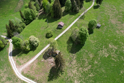 Aerial view of a winding dirt path crossing through lush green meadows with small wooden huts and scattered trees Rougemont Vaud Switzerland. Aerial view of a winding dirt path crossing through lush green meadows with small wooden huts and scattered trees Rougemont Vaud Switzerland.