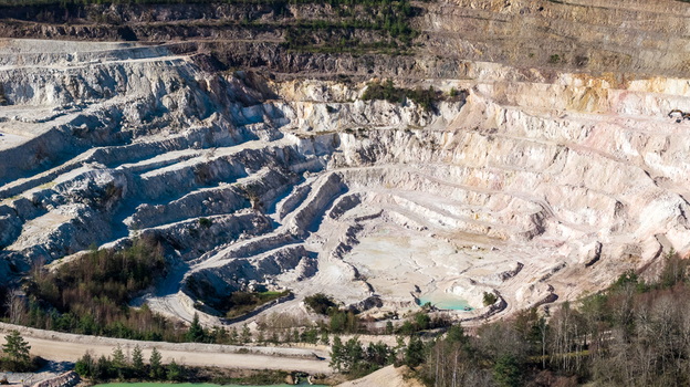 Aerial view of the stark white quarry s terraced levels contrasting with the surrounding green trees &Eacute;chassi&egrave;res Auvergne Rh&ocirc;ne Alpes France.