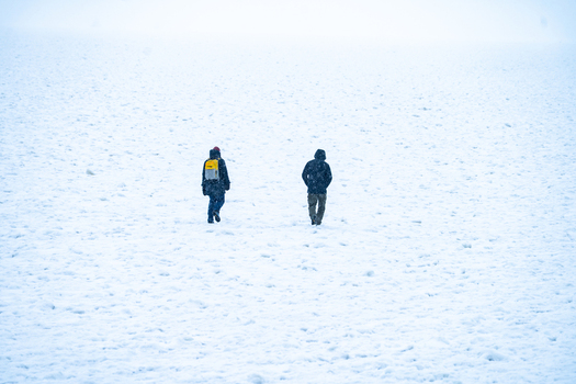 View of two people walking across a vast snow covered surface during a winter day in Sassnitz Mecklenburg Vorpommern Germany.