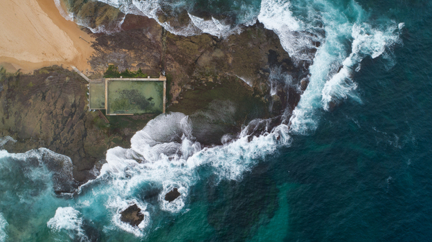 Aerial view of Newport Rock Pool on the rocky coastline with crashing turquoise waves and sandy beach in Sydney New South Wales Australia.