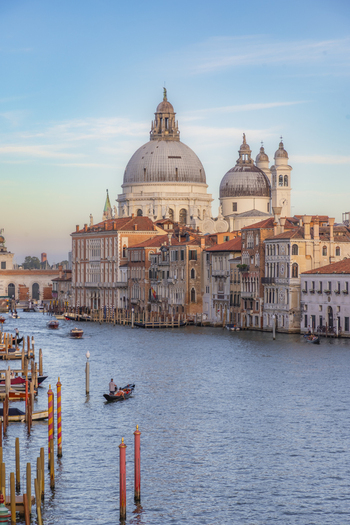 View of Santa Maria della Salute basilica with its iconic domes rising above the Grand Canal featuring historic buildings wooden mooring poles and a gondola in Venice Veneto Italy. View of Santa Maria della Salute basilica with its iconic domes rising above the Grand Canal featuring historic buildings wooden mooring poles and a gondola in Venice Veneto Italy.