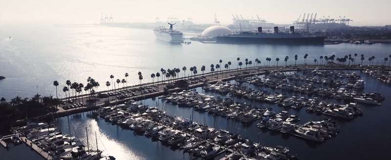 Aerial view of the marina in Long Beach with docked boats palm trees and the historic Queen Mary ship and cruise liner in Los Angeles California United States.