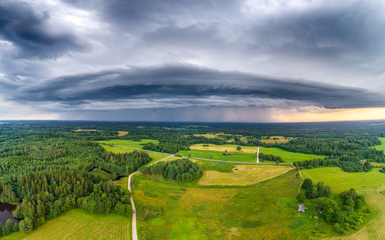 Aerial view of a dramatic shelf cloud hanging over the lush green fields and dense forests of the Latvian countryside in Latvia. Aerial view of a dramatic shelf cloud hanging over the lush green fields and dense forests of the Latvian countryside in Latvia.