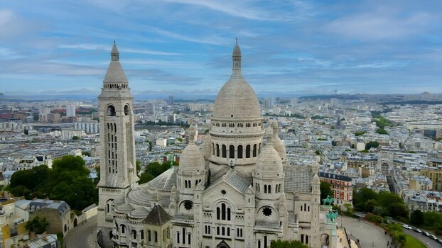 Aerial view of the Sacre Coeur Basilica in Montmartre featuring its white stone domes bell tower and the sprawling cityscape of Paris. Paris Ile de France France. Aerial view of the Sacre Coeur Basilica in Montmartre featuring its white stone domes bell tower and the sprawling cityscape of Paris. Paris Ile de France France.