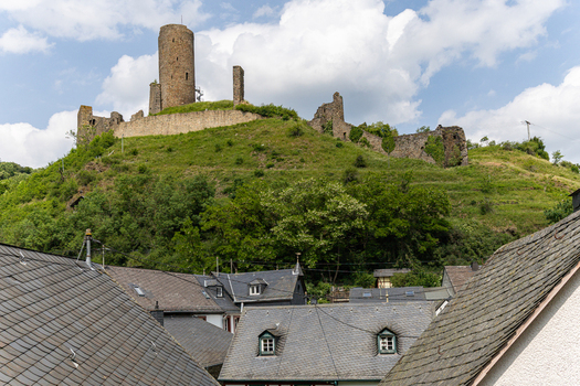 View of the historic Monreal Castle ruins on a lush green hill above traditional slate rooftops under a cloudy sky in Monreal Rheinland Pfalz Germany. View of the historic Monreal Castle ruins on a lush green hill above traditional slate rooftops under a cloudy sky in Monreal Rheinland Pfalz Germany.