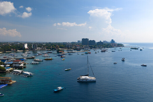Lapu Lapu Philippines 15 May 2026 Aerial view of numerous outrigger boats and a catamaran anchored in the turquoise waters along the urban coastline under a bright blue sky. Lapu Lapu Philippines 15 May 2026 Aerial view of numerous outrigger boats and a catamaran anchored in the turquoise waters along the urban coastline under a bright blue sky.