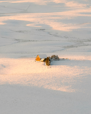 Aerial view of a solitary typical buron house in a snow covered landscape the golden light casting long shadows across the pristine white expanse Nasbinals Occitanie France.