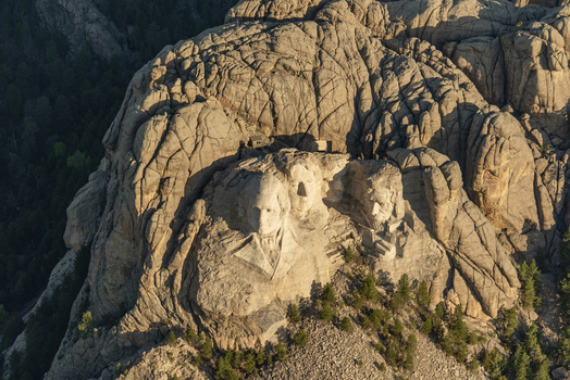 Aerial view of Mount Rushmore National Memorial featuring the carved faces of US presidents on granite rock surrounded by pine forests in Keystone South Dakota United States. Aerial view of Mount Rushmore National Memorial featuring the carved faces of US presidents on granite rock surrounded by pine forests in Keystone South Dakota United States.