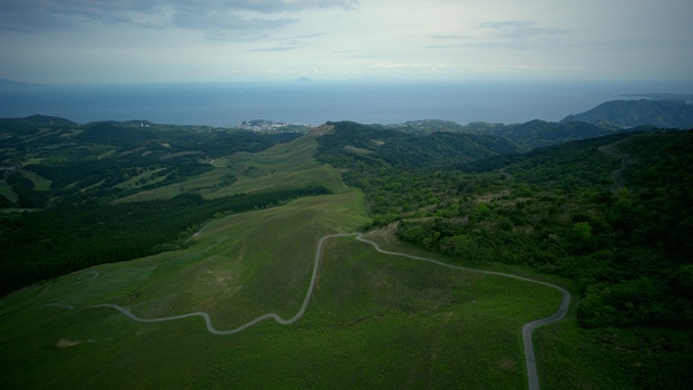 Aerial view of Hosono Plateau featuring rolling green hills and winding roads with the Pacific Ocean in the background in Higashiizu Shizuoka Japan. Aerial view of Hosono Plateau featuring rolling green hills and winding roads with the Pacific Ocean in the background in Higashiizu Shizuoka Japan.