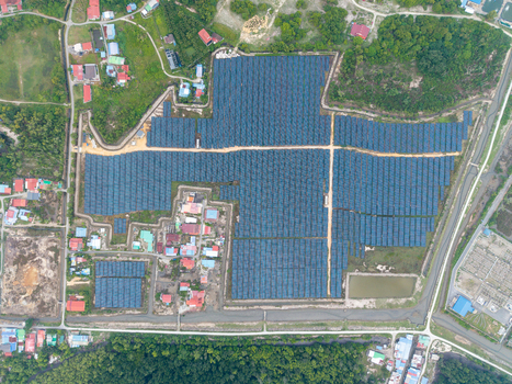 Aerial view of a large scale solar photovoltaic power plant with rows of panels surrounded by houses roads and vegetation in Central Seberang Perai Penang Malaysia. Aerial view of a large scale solar photovoltaic power plant with rows of panels surrounded by houses roads and vegetation in Central Seberang Perai Penang Malaysia.