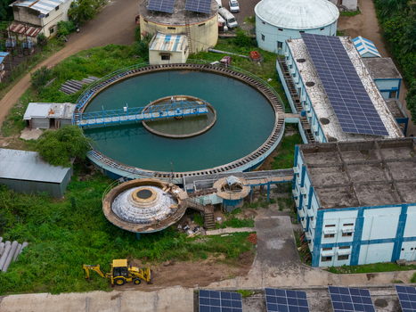 Aerial view of a water treatment plant featuring circular sedimentation tanks and solar panels on rooftops with a yellow construction vehicle parked nearby in Karad Maharashtra India.