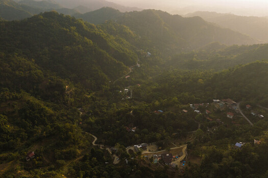 Aerial view of Busay hills with lush tropical vegetation and scattered houses under a hazy golden light in Cebu City Central Visayas Philippines.