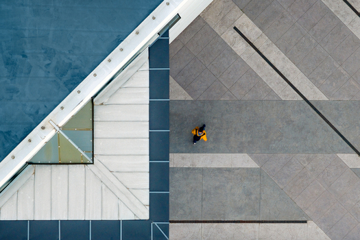 Aerial view of a person in a yellow jacket walking across a geometric paved plaza next to a modern building roof in Belgrade City of Belgrade Serbia. Aerial view of a person in a yellow jacket walking across a geometric paved plaza next to a modern building roof in Belgrade City of Belgrade Serbia.