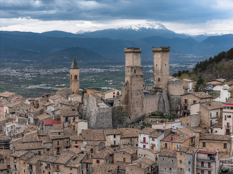 Aerial view of the medieval Caldora Castle and historic stone houses under a dramatic cloudy sky with snow capped mountains in the distance in Pacentro Abruzzo Italy. Aerial view of the medieval Caldora Castle and historic stone houses under a dramatic cloudy sky with snow capped mountains in the distance in Pacentro Abruzzo Italy.