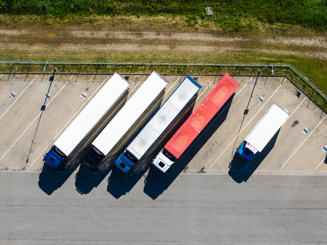 Aerial view of several semi trucks parked in a row at a logistics facility with white blue and red trailers casting long shadows on the asphalt in Lielvarzi Kekava Municipality Latvia. Aerial view of several semi trucks parked in a row at a logistics facility with white blue and red trailers casting long shadows on the asphalt in Lielvarzi Kekava Municipality Latvia.