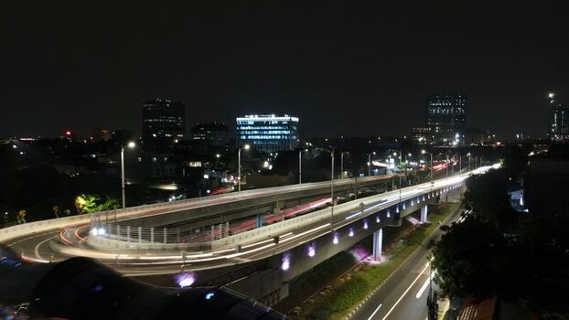 Aerial view of Flyover Tapal Kuda Jakarta at night with light trails from traffic modern urban infrastructure and city buildings in Pasar Minggu Daerah Khusus Ibukota Indonesia. Aerial view of Flyover Tapal Kuda Jakarta at night with light trails from traffic modern urban infrastructure and city buildings in Pasar Minggu Daerah Khusus Ibukota Indonesia.