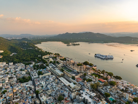 Aerial view of the historic City Palace complex situated on the banks of Lake Pichola with surrounding urban architecture and distant Aravalli hills in Udaipur Rajasthan India.