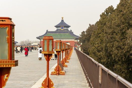 View of the Temple of Heaven with traditional red lanterns lining a stone walkway and people walking under a hazy sky Beijing Beijing China. View of the Temple of Heaven with traditional red lanterns lining a stone walkway and people walking under a hazy sky Beijing Beijing China.