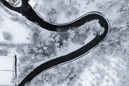 Aerial view of a winding asphalt road cutting through a dense snow covered forest with evergreen trees in Rivisondoli Abruzzo Italy.