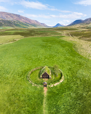 Aerial view of a traditional Icelandic turf church surrounded by a circular stone wall in a vast green field with mountains in the background Iceland. Aerial view of a traditional Icelandic turf church surrounded by a circular stone wall in a vast green field with mountains in the background Iceland.