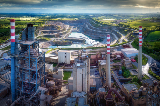 Aerial view of the Irish Cement Ltd facility featuring tall chimneys and a vast open pit quarry surrounded by green fields in Drogheda County Louth Ireland. Aerial view of the Irish Cement Ltd facility featuring tall chimneys and a vast open pit quarry surrounded by green fields in Drogheda County Louth Ireland.