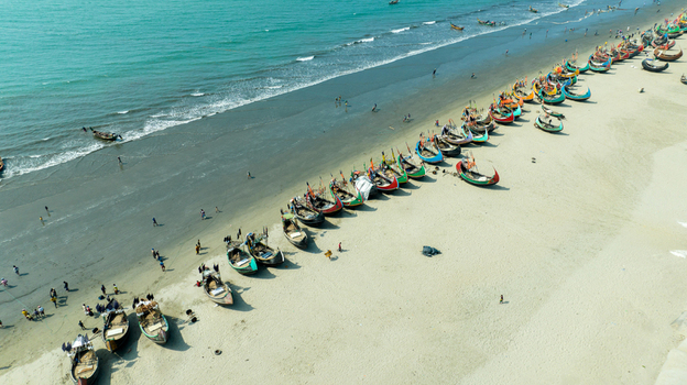 Aerial view of vibrant fishing boats rest on the sandy shore where the turquoise sea meets the land Cox s Bazar Chittagong Division Bangladesh. Aerial view of vibrant fishing boats rest on the sandy shore where the turquoise sea meets the land Cox s Bazar Chittagong Division Bangladesh.