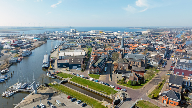 Aerial view of the historic town center featuring a prominent church spire a canal with boats and industrial harbor facilities under a clear sky in Lemmer Friesland Netherlands.