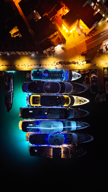 Aerial view of luxury yachts docked at a pier at night with vibrant underwater lighting and warm city lights in Vis Split Dalmatia County Croatia. Aerial view of luxury yachts docked at a pier at night with vibrant underwater lighting and warm city lights in Vis Split Dalmatia County Croatia.