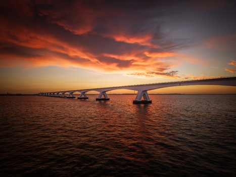 Aerial view of the Zeeland Bridge spanning the water under a dramatic sunrise sky with vibrant orange clouds in Zierikzee Zeeland Netherlands. Aerial view of the Zeeland Bridge spanning the water under a dramatic sunrise sky with vibrant orange clouds in Zierikzee Zeeland Netherlands.