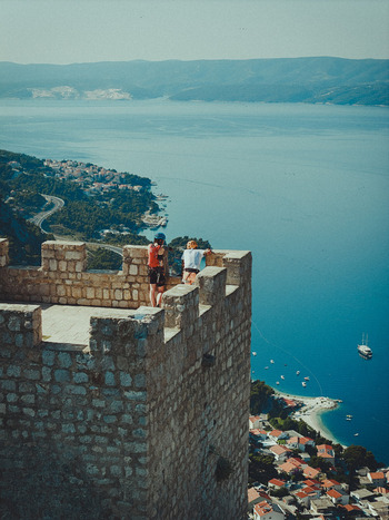 Aerial view of two people standing on the stone ramparts of the historic fortress overlooking the Adriatic Sea and the coastal town of Omis Split Dalmatia County Croatia. Aerial view of two people standing on the stone ramparts of the historic fortress overlooking the Adriatic Sea and the coastal town of Omis Split Dalmatia County Croatia.