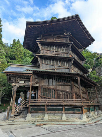 View of the historic Sazae do wooden temple with its unique double helix structure and visitors entering surrounded by lush trees under a blue sky in Aizuwakamatsu Fukushima Japan.