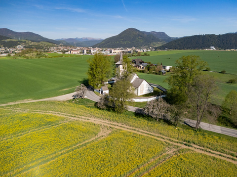 Aerial view of the historic All Saints Church surrounded by a stone wall lush green fields and yellow rapeseed blossoms under a clear blue sky in Ludrova Zilina Region Slovakia. Aerial view of the historic All Saints Church surrounded by a stone wall lush green fields and yellow rapeseed blossoms under a clear blue sky in Ludrova Zilina Region Slovakia.
