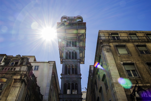 View of the neo Gothic Santa Justa Lift tower rising between historic buildings under a bright sun with lens flare in Lisbon Lisbon Portugal. View of the neo Gothic Santa Justa Lift tower rising between historic buildings under a bright sun with lens flare in Lisbon Lisbon Portugal.