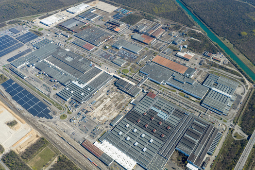 Aerial view of a sprawling industrial complex with geometric rooftops and solar panels casting shadows in the afternoon sun Sausheim Grand Est France.