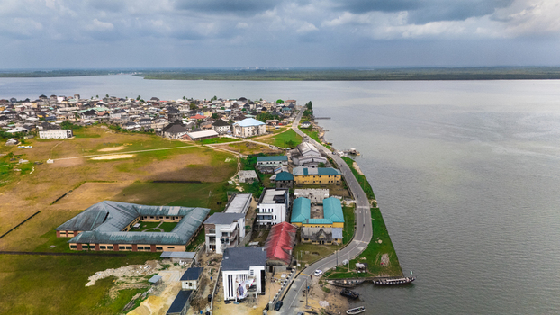 Aerial view of a coastal settlement featuring residential buildings a school complex a winding road along the riverbank and small boats in Rivers Nigeria.