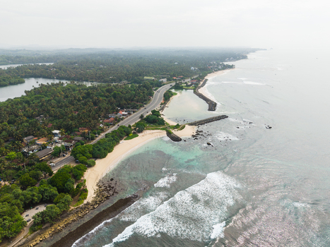 Aerial view of the tropical coastline with sandy beaches turquoise ocean waves and a coastal road winding through lush palm trees in Koggala Southern Province Sri Lanka. Aerial view of the tropical coastline with sandy beaches turquoise ocean waves and a coastal road winding through lush palm trees in Koggala Southern Province Sri Lanka.