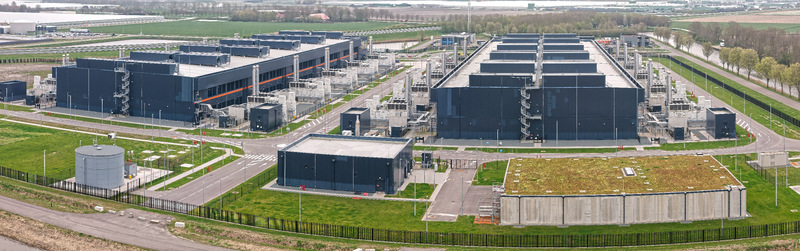 Aerial view of a large modern data center campus with dark industrial buildings rows of back up energy generators and green surroundings in Middenmeer Noord Holland Netherlands.